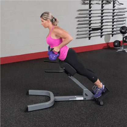 Frau trainiert mit Kettlebell auf Hantelbank im Fitnessstudio – Krafttraining & Homegym Equipment