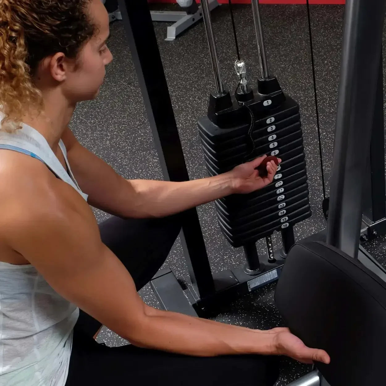 Frau justiert Gewicht an Kraftstation im Fitnessstudio – ideales Homegym Equipment für Krafttraining