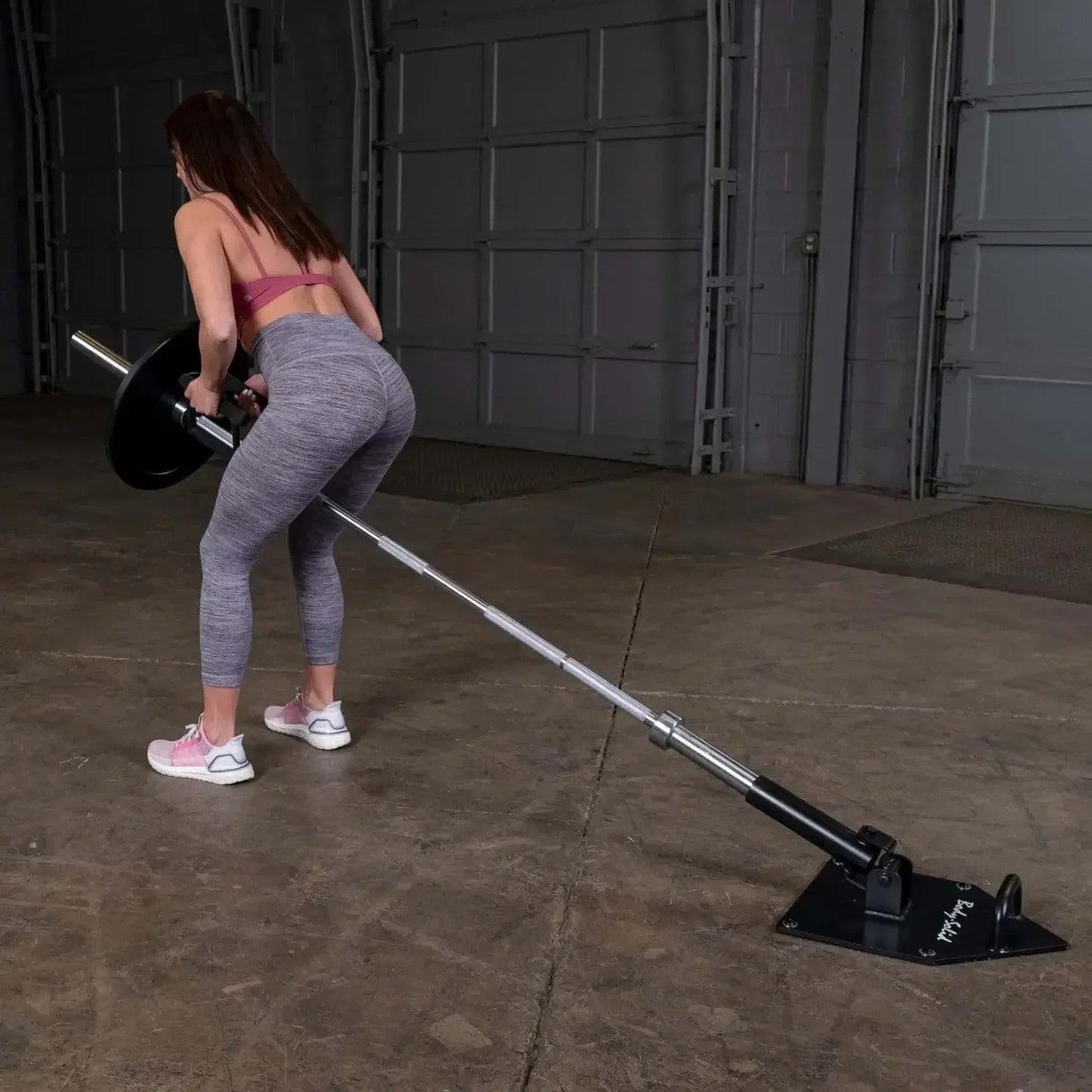 Frau trainiert mit Langhantel und Bodenanker im Homegym – Kraftsport Equipment für effektives Training