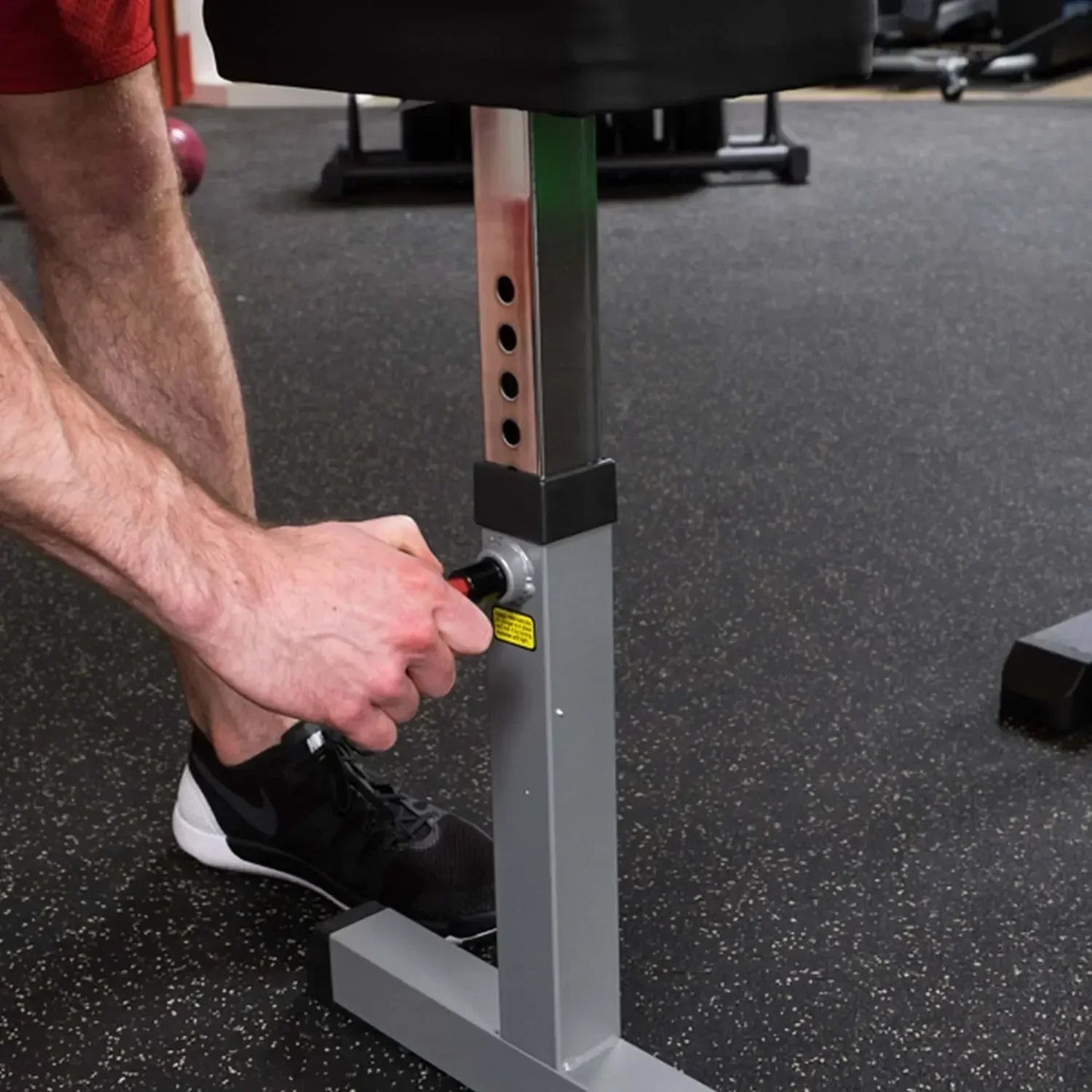 Mann justiert Hantelbank mit Höhenverstellung im Fitnessstudio