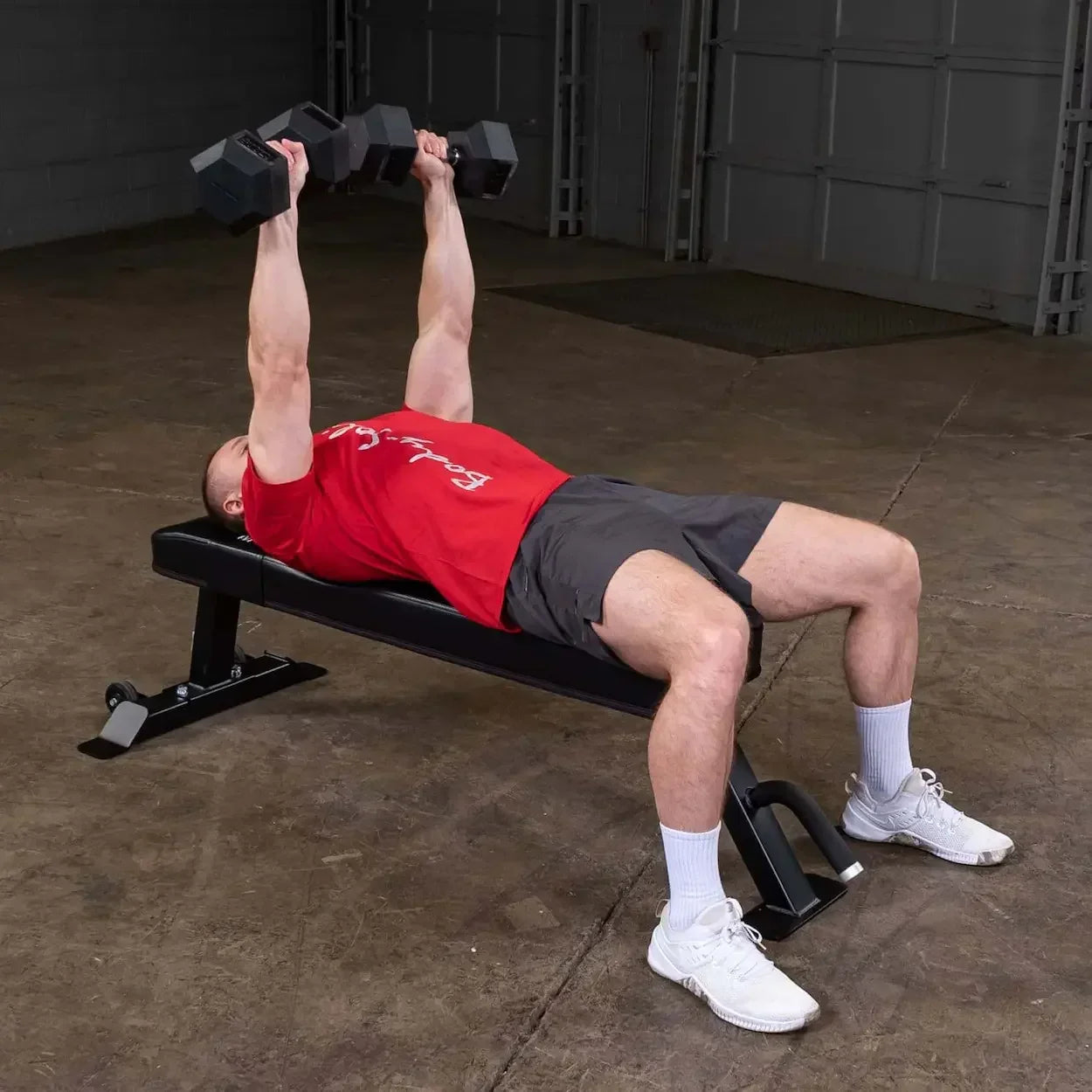 Mann trainiert mit Hanteln auf Hantelbank im Fitness-Studio