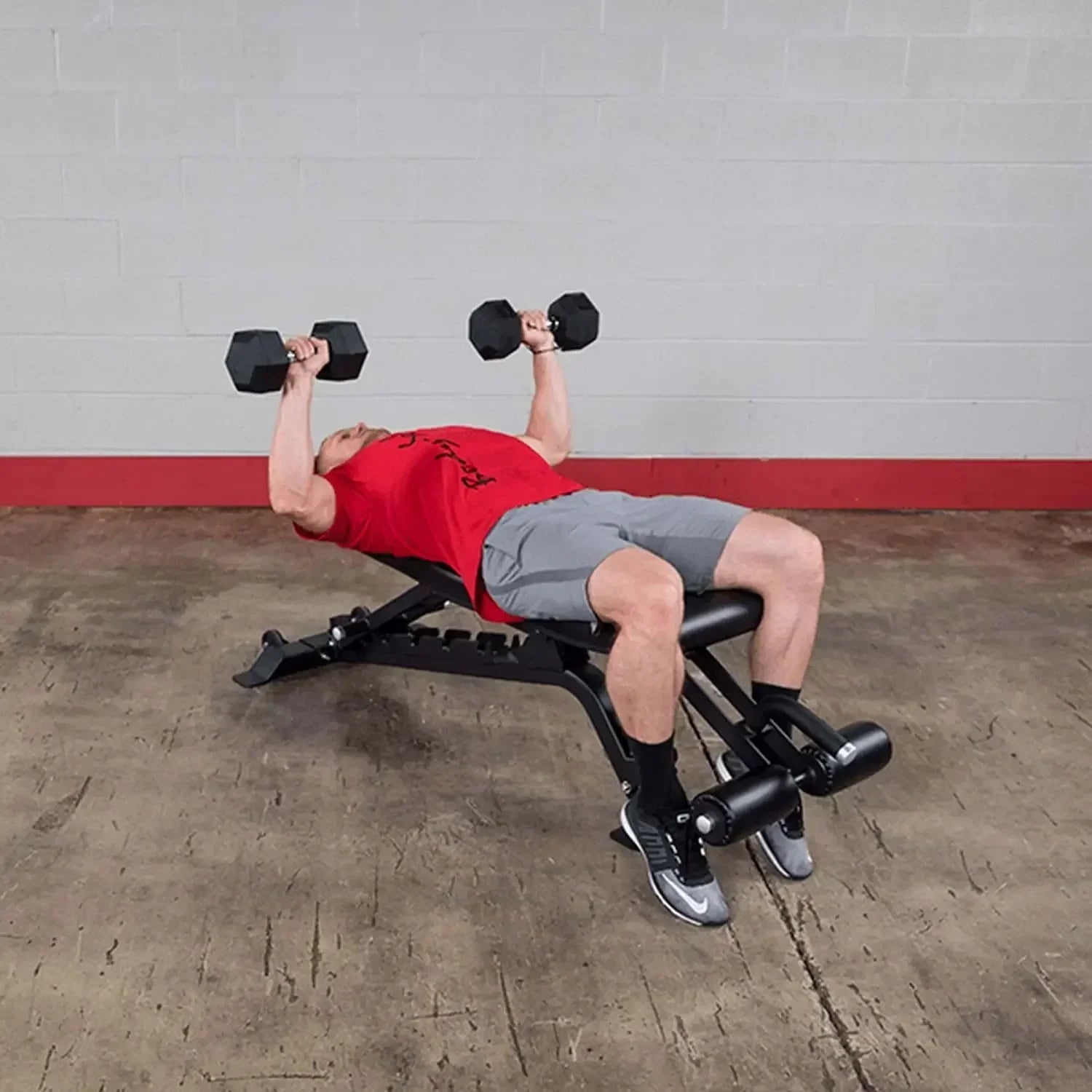 Mann trainiert mit Hanteln auf Hantelbank im Fitnessstudio – ideales Equipment für Homegym & Studio